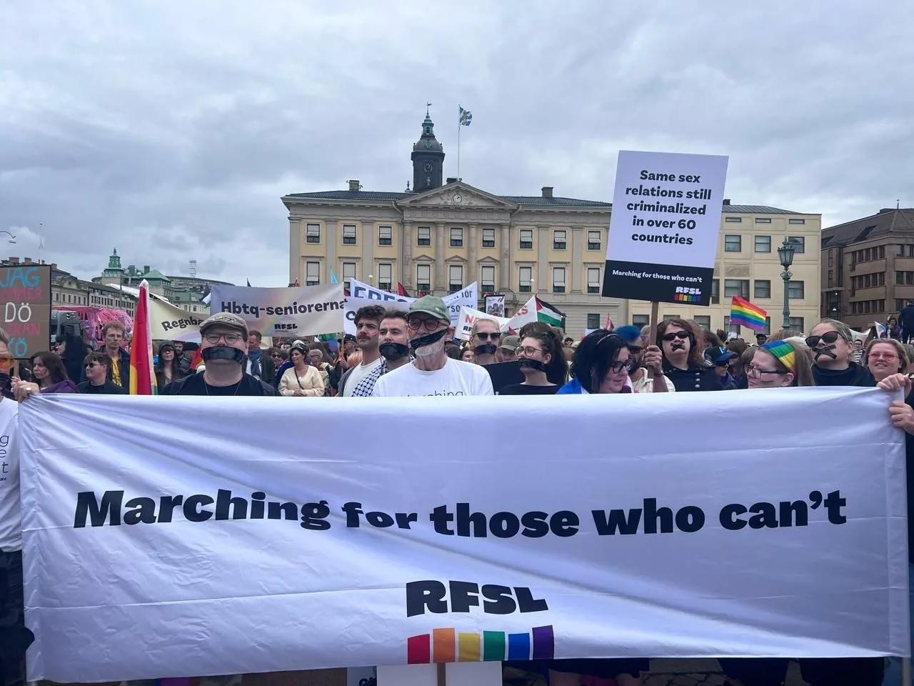 People are marching in the Pride parade with a banner that reads "Marching for those who can't"