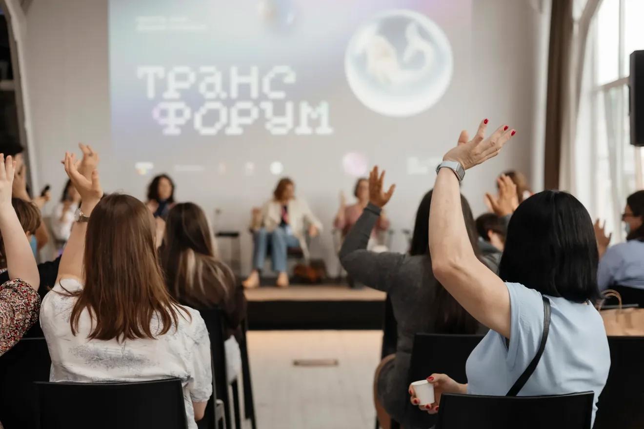 A photo taken in the auditorium during a panel discussion at Trans Forum 2026. In the photo, people in the audience are giving "silent applause."